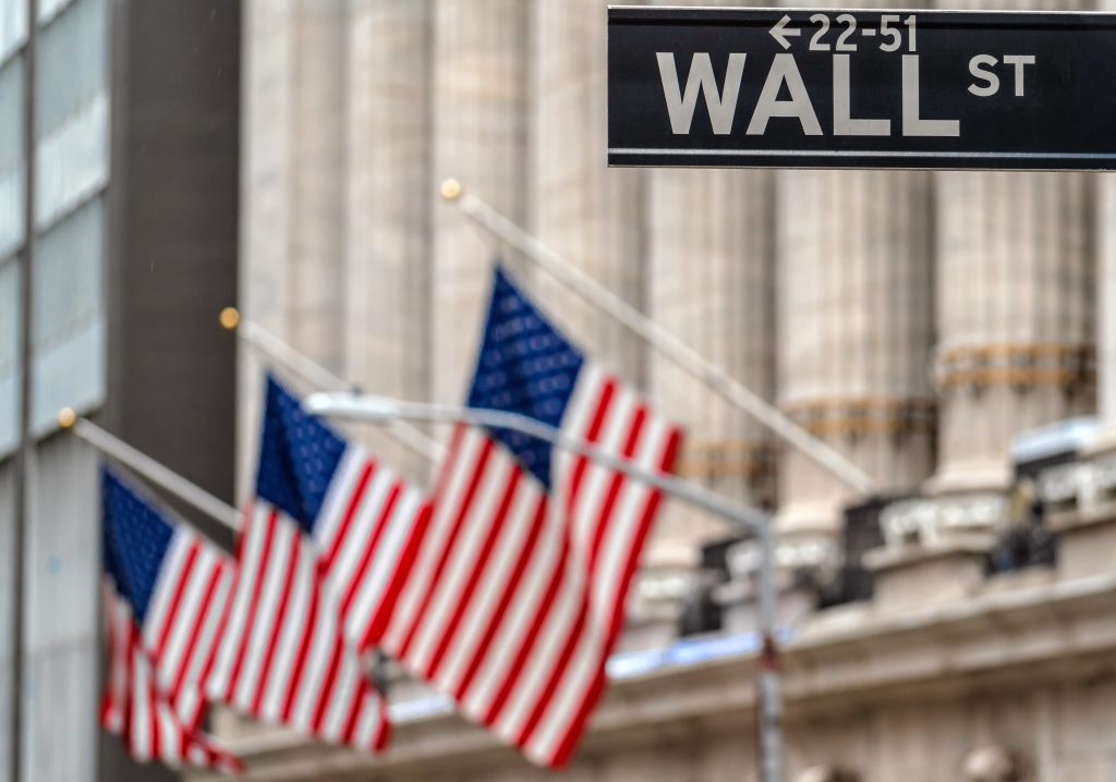 Wall Street sign with American flags in front of NYSE building